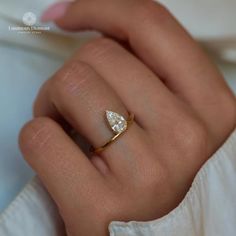 a woman's hand wearing a gold ring with a pear shaped diamond on it