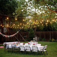 an outdoor party setup with tables, chairs and string lights strung from the trees in the back yard