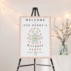 a welcome sign is on an easel next to a vase with flowers in it