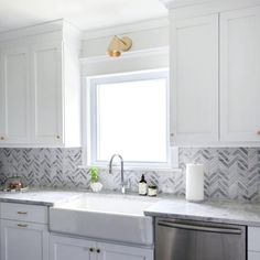 a white kitchen with marble counter tops and gold hardware on the faucet above the sink