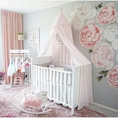 a baby's room decorated in pink and gray with flowers on the wall, crib, rocking chair, cot