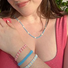 a woman wearing two bracelets and a pink top is posing for the camera with her hand on her chest