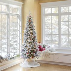 a decorated christmas tree in the corner of a room next to two windows with snow on them