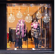 two mannequins dressed in winter clothes are seen through the glass windows of a clothing store