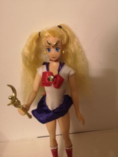 a doll with blonde hair and blue dress holding a gold object in her hand,