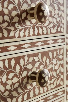 the drawers are decorated with intricate designs and knobs on each drawer, which is painted in brown and white