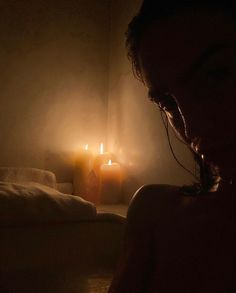 a person sitting in a dimly lit room next to a bed with candles on it