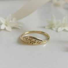 a close up of a gold ring on a white surface with flowers in the background