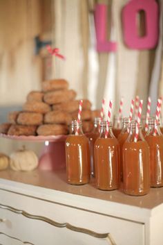 there are many bottles with straws in them on the table next to donuts