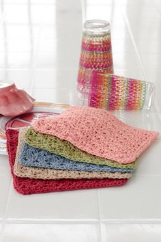 four crocheted dishcloths are sitting on the floor next to a vase