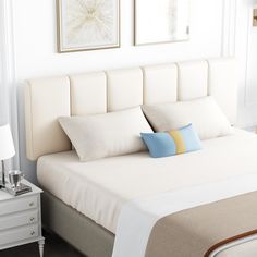 a white bed with two blue and yellow pillows on it's headboard next to a night stand