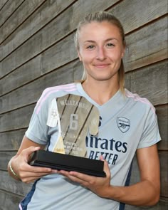 a female soccer player holding an award in front of a wooden wall with her name on it