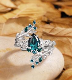 a ring with green and white stones on top of some leafy leaves in the background