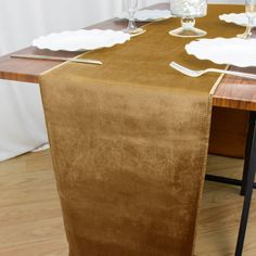 a brown table runner with white plates and silverware on it in front of a curtain