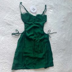 a green dress laying on top of a white bed next to a tag that says,