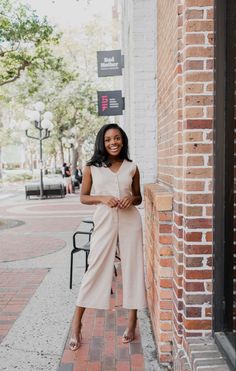 a woman standing on the sidewalk in front of a brick building smiling at the camera