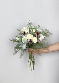 a person holding a bouquet of flowers with pine cones and greenery on the stems