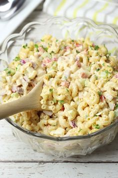 a glass bowl filled with macaroni salad and a wooden spoon