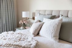 a white bed with pillows and blankets on top of it next to a window covered in curtains