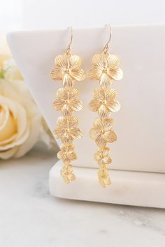 the gold flower earrings are on display next to a white vase with flowers in it