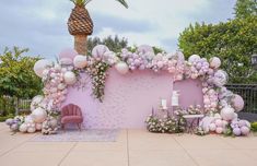 a pink wall with balloons, flowers and a palm tree in the middle is decorated