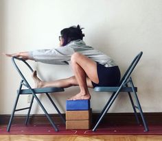 a woman sitting on top of a blue chair next to a wooden box in front of a white wall