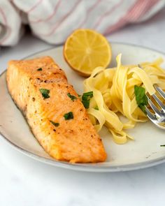 a white plate topped with salmon and pasta next to a lemon wedge on a table