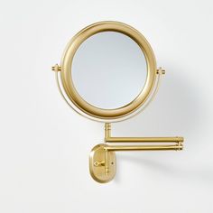 a gold wall mounted magnifying mirror on a white wall next to a hook