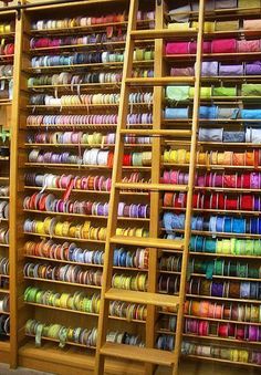 many different colored spools of thread are on display in a store with wooden shelves