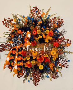 a wreath with happy fall written on it and oranges, yellows, and blue flowers