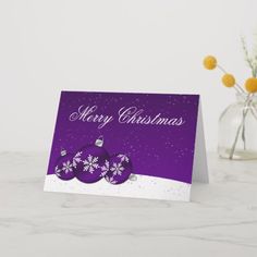 a purple christmas card sitting on top of a table next to a vase filled with flowers