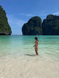 a woman is standing in the water near some mountains and rocks, with her head turned to the side