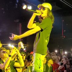 a man in green shirt and yellow pants standing on stage with microphones to his side