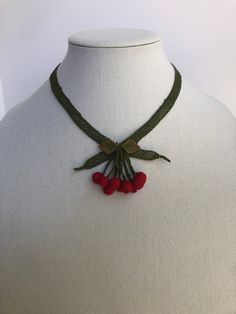 a white mannequin wearing a green and red necklace with cherries on it