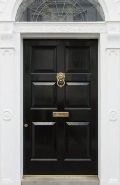 a black front door with a gold knocker on it's side and an arched glass window