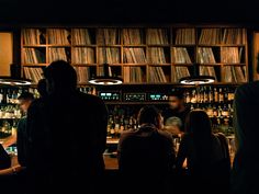 a group of people standing in front of a bar filled with liquor bottles and records