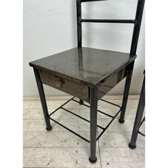 an old metal chair sitting next to a wooden table with a drawer on the bottom