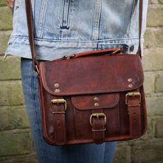 "This is our timeless classic version of the traditional leather satchel.  Made naturally from goat hide, this bag ages beautifully, becoming softer and more organic with use.   This bag has two press-in buckles and a pocket on the front which closes with a magnetic button. Inside the bag, which is lined with canvas, there are two separate compartments and a zipped compartment. The zipped pocket on the back of the bag makes this bag practical as well as safe. The shoulder strap with a traditional belt-buckle design makes it simple to adjust to your preferred length. Measurements: Height:18cm/7\"  Width:  23cm/9\"  Depth:  8cm/3\" Max Shoulder Strap Lenght: 140cm/55\"" Everyday Satchel Saddle Bag With Buckle Closure, Leather Satchel Saddle Bag With Buckle Closure, Leather Saddle Bag With Buckle Closure, Leather Saddle Bag With Buckle Closure Satchel, Rectangular Saddle Bag With Buckle Closure For Everyday Use, Vintage Leather Satchel With Waxed Finish, Satchel With Buckle Closure For Daily Use, Vintage Waxed Finish Satchel Bag, Vintage Satchel With Waxed Finish