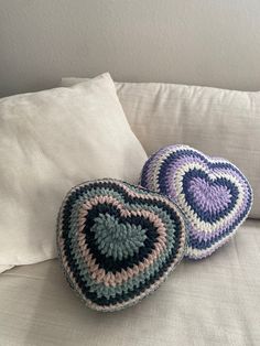 two crocheted hearts sitting on top of a white pillow next to each other