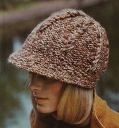 a woman wearing a brown knitted hat next to a body of water with trees in the background