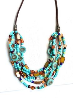 a multi stranded necklace with beads and charms on a brown cord, hanging from a white wall