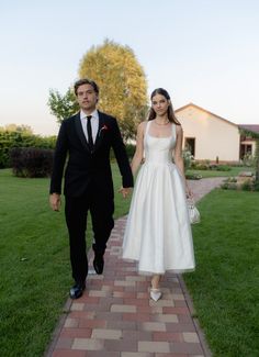 a man and woman walking down a brick path together in formal wear, holding hands