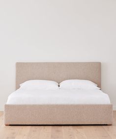 a bed with white sheets and pillows on top of the headboard in a room