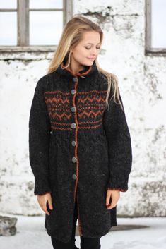 a woman standing in the snow wearing a black coat with an orange pattern on it