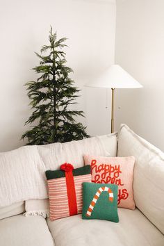 a white couch with christmas pillows on it and a small tree in the corner next to it