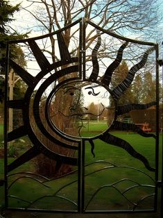 a metal gate with a sun design on it's face and trees in the background