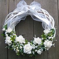 a wreath with white flowers and greenery is hanging on a wooden wall, ready to be used as a decoration