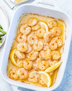 a casserole dish filled with shrimp and lemons next to asparagus