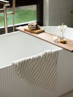 a white bath tub sitting under a window next to a wooden tray with towels on it