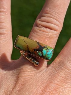 This is a dainty polychrome turquoise bar from the Qingu mine in Bamboo Mountain county. This mining district produces some of the widest color ranges. This piece is stabilized, so it has a sheen to it. The latte brown bar darkens into milk chocolate before popping into turquoise. It's placed horizontally for a little twist to the traditional bar ring.  The gold band is a a braided tail style. It's been electroformed with 40 mils of 24K gold. It should not rub off, tarnish, or flake off for many decades with careful wear. It's coming to a size 5 on the ring sizer. Dimensions: 0.92 x 0.32 inches (23.4 x 8.1 mm) Ring Weight: 0.16 ounces (4.6 grams) Turquoise is one of the oldest healing stones and has been a symbol of wisdom, nobility, and immortality for thousands of years. It corresponds t Rectangular Turquoise Gemstone Ring, Unique Rectangular Turquoise Ring, Artisan Rectangular Green Jewelry, Artisan Green Rectangular Jewelry, Green Rectangular Artisan Jewelry, Unique Green Rectangular Jewelry, Unique Green Rectangular Rings, Traditional Bar, Turquoise Bar